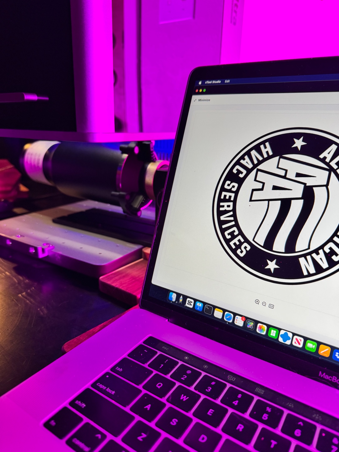 Logo design displayed on laptop screen beside the laser machine with pink studio lighting